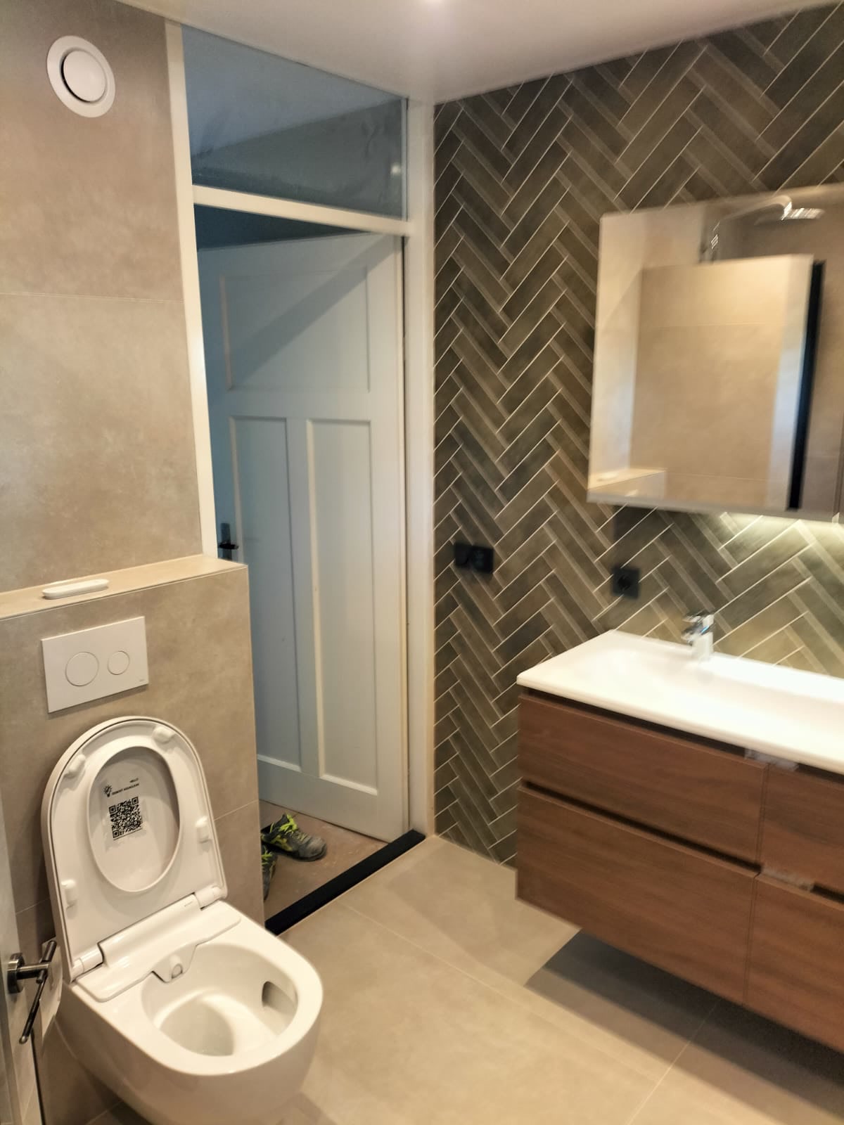 Badkamer met visgraat tegelwand, zwevend toilet en houten meubel
